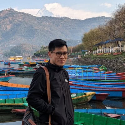 Khai-Thai steht am Phewa-See in Pokhara, Nepal, mit bunten Holzbooten und dem Annapurna-Massiv im Hintergrund – Profilbild für den meinNepal Blog.