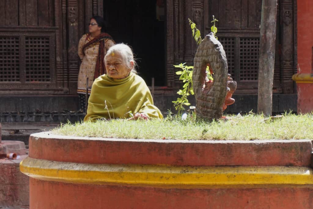 Ältere Frau sitzt in Kathmandu ruhig am Tempel, Symbol für Gelassenheit im Kontrast zum hektischen Stadtleben