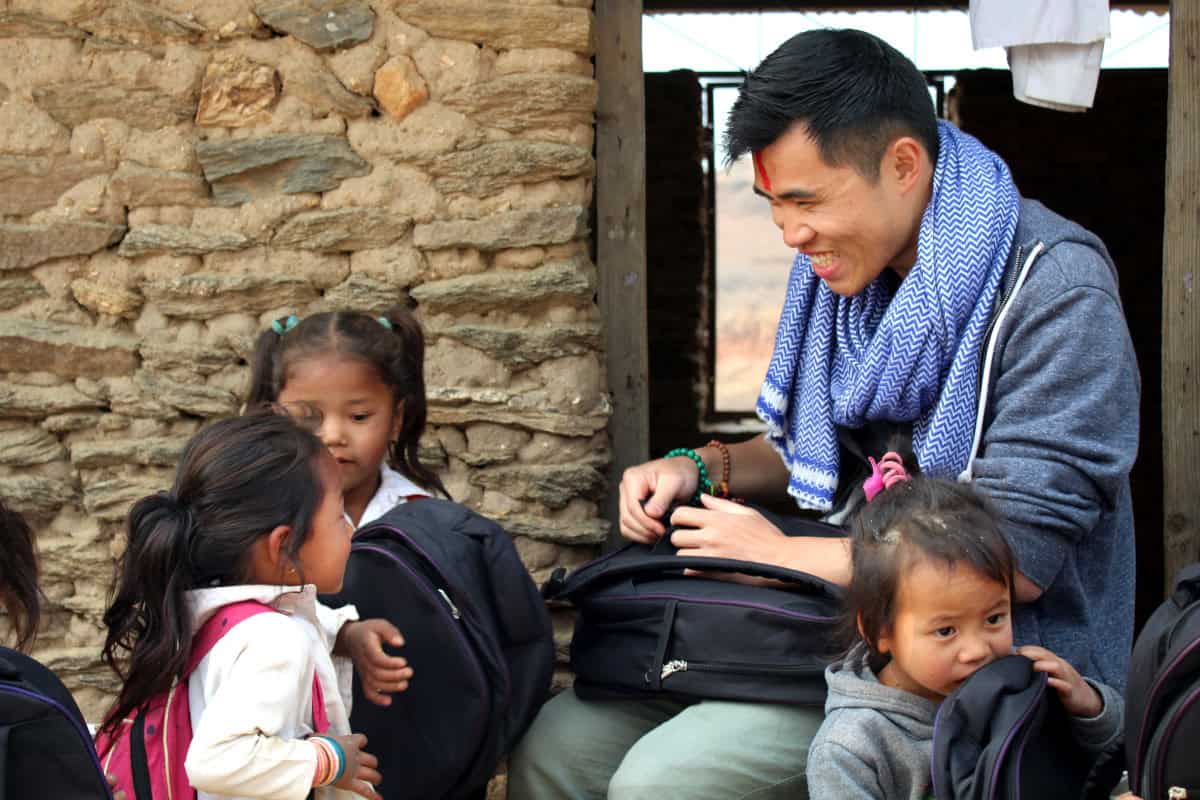 Khai-Thai, der Gründer von meinNepal, verteilt in Nepal mit einem Lächeln Schultaschen an Kinder in einer entlegenen Bergregion.