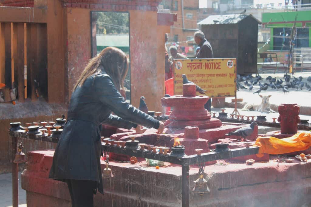 Frau entzündet Opfergaben an einem hinduistischen Schrein in Nepal, Religion als Teil der Kultur
