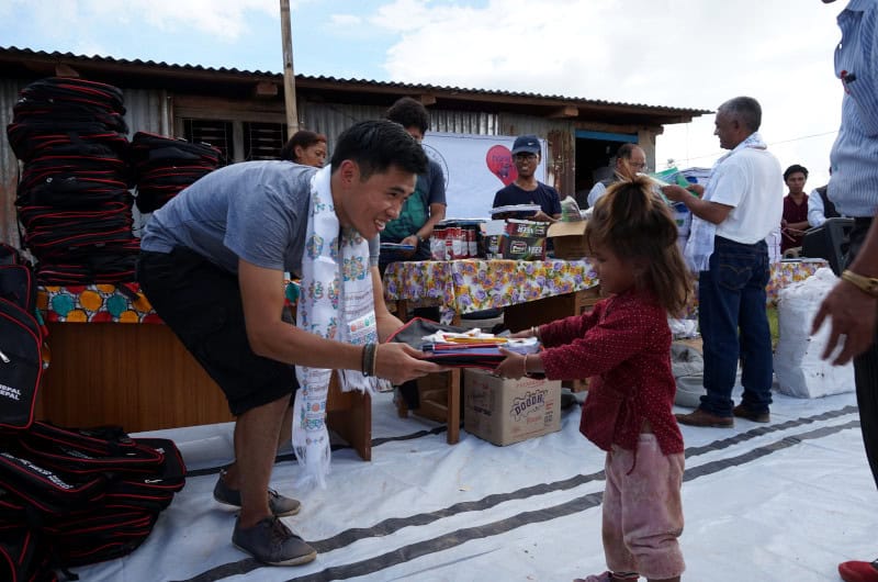 Ein Vereinsmitglied von hamromaya Nepal e.V. übergibt einem nepalesischen Mädchen in einem abgelegenen Dorf Schulmaterialien.
