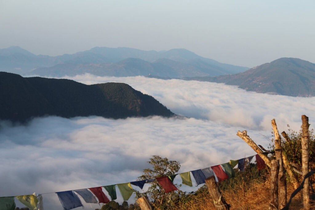 Südlicher Morgenblick vom Australian Basecamp nahe Pokhara über ein Wolkenmeer und die Hügel des Himalaya mit Gebetsfahnen im Vordergrund