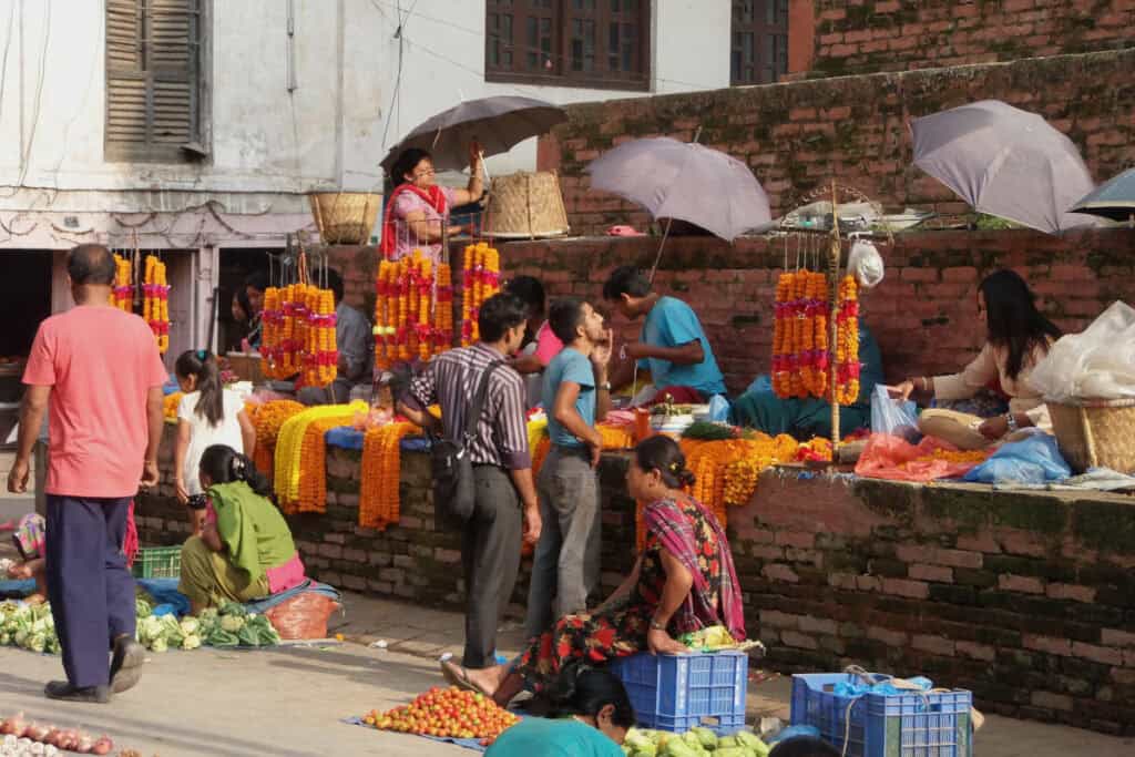 Buntes Markttreiben in Kathmandu mit Gemüse, Blumen und Menschen in traditionellen und modernen Kleidern – Begegnung von Tradition und Moderne