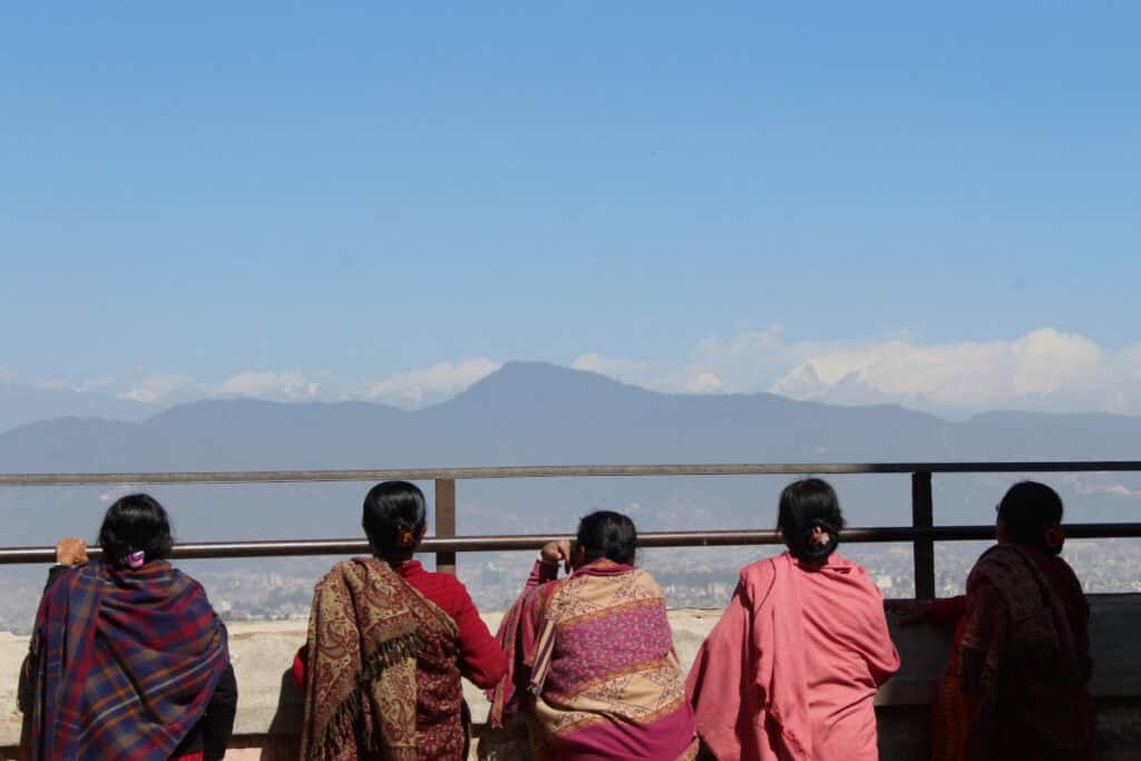 Fünf nepalesische Frauen in bunten Schals blicken ruhig auf die Berge des Himalaya – ein Symbol für Gelassenheit und das Leben im Moment.