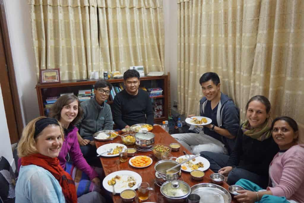 Gäste, Nachbarn und Teammitglieder von Project Volunteer Nepal sitzen beim gemeinsamen Abendessen in der Unterkunft in Kathmandu – Begegnungen voller Wärme und Authentizität.