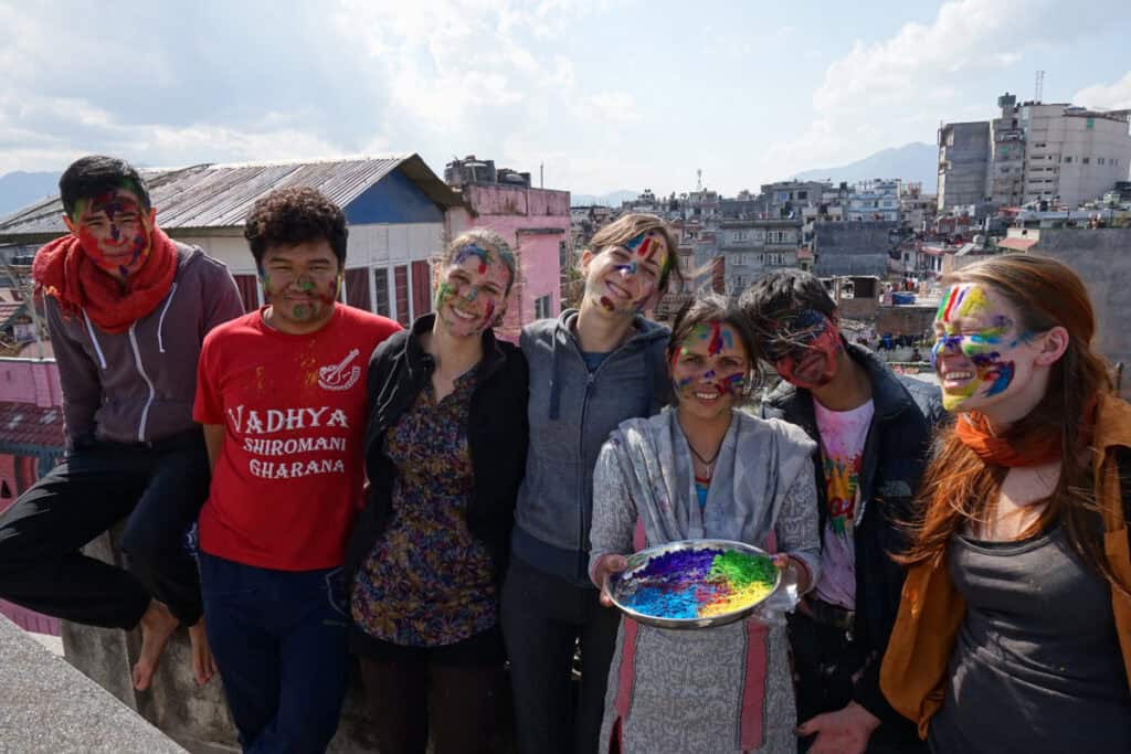 Farbverschmierte Gesichter lachender Menschen während des Holi-Festes 2017 in Kathmandu – Volunteers und nepalesische Nachbarn feiern gemeinsam auf einer Dachterrasse