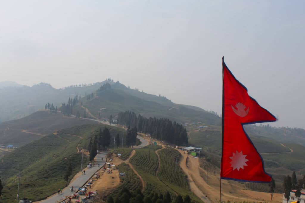 Die nepalesische Flagge weht über den grünen Hügeln im Distrikt Ilam – ein Symbol für den Stolz und die Eigenständigkeit des Landes.