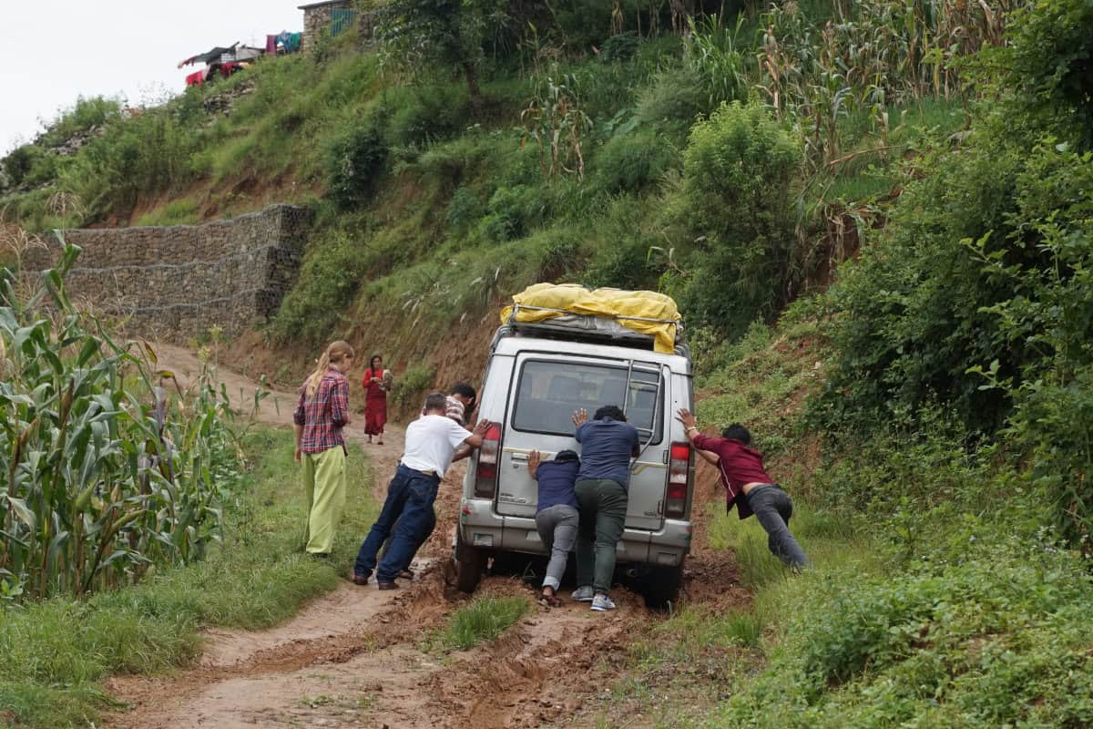 Menschen schieben in Nepal einen Jeep auf einer schlammigen Bergstraße während einer Projektreise