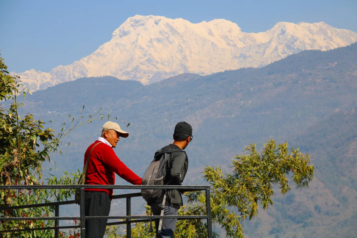 Zwei Menschen blicken von einem Aussichtspunkt in Nepal auf den schneebedeckten Himalaya – klare Luft und strahlender Himmel in der besten Reisezeit