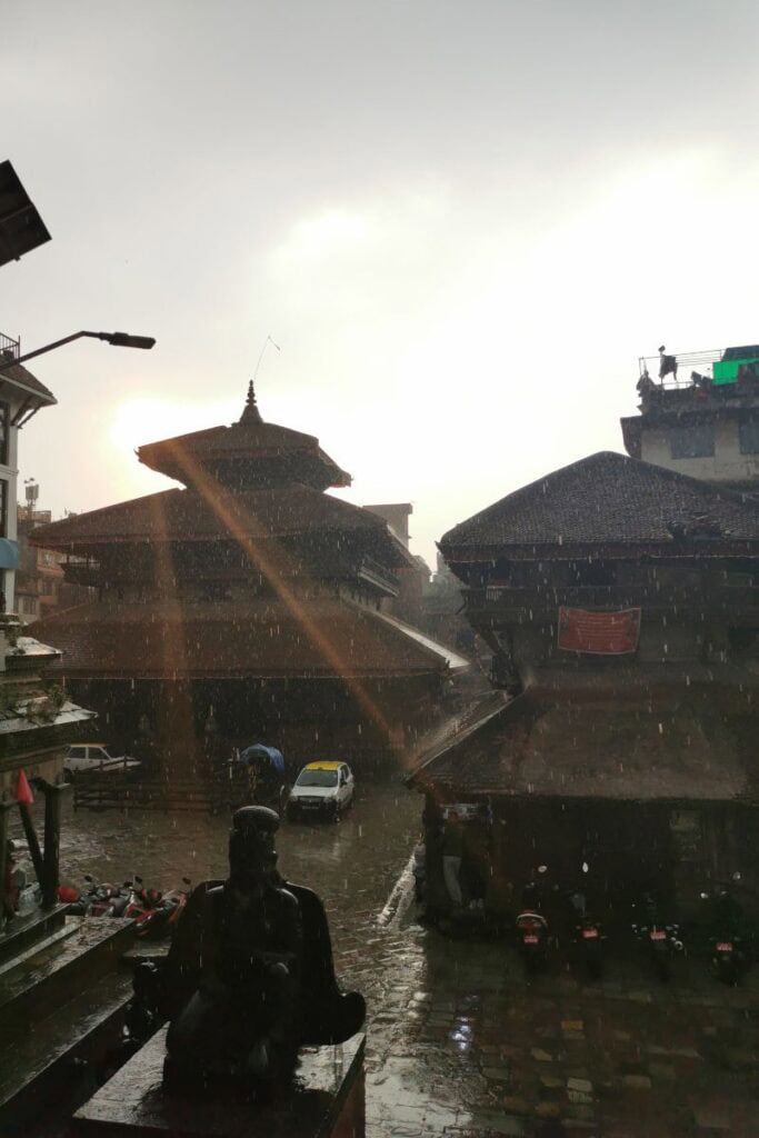 Historische Malla-Architektur am Kathmandu Durbar Square im Regen, mit Sonnenstrahlen über den Pagoden-Tempeln.