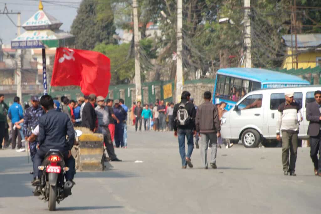 Politische Straßenblockade während eines Bandhs in Kathmandu – Menschen mit roter Fahne, Polizei und Motorradfahrer auf leerer Straße.