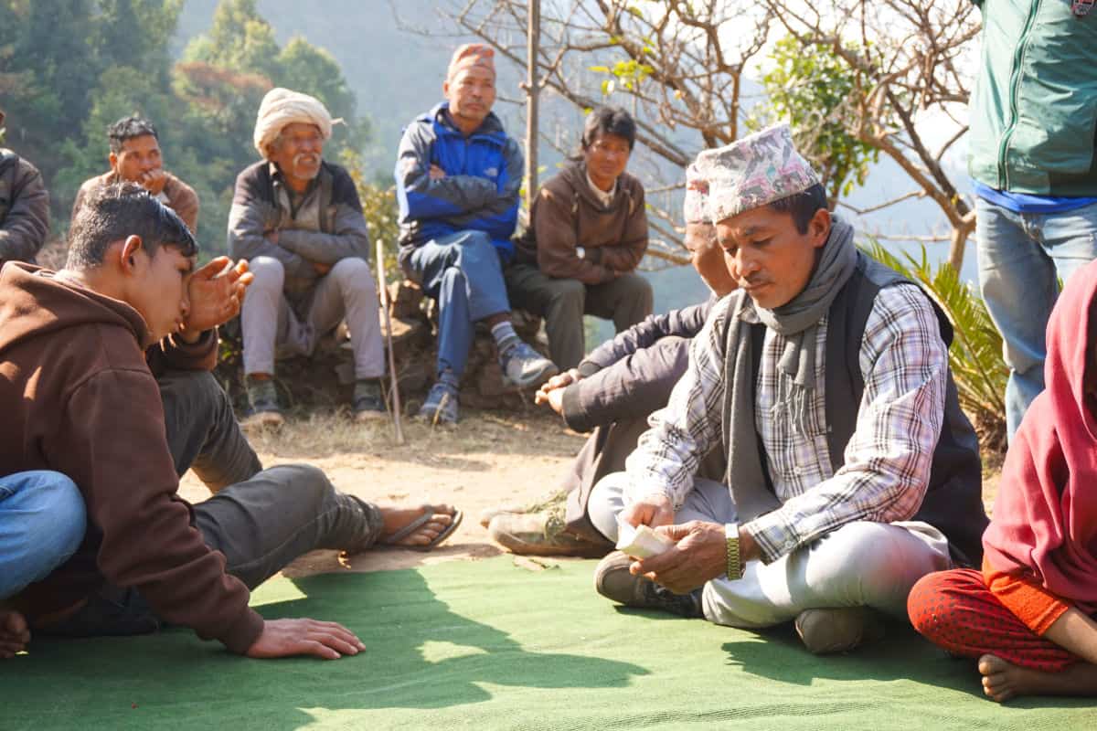 Männer und Jugendliche sitzen gemeinsam auf dem Boden in einem nepalesischen Dorf – eine typische Szene des gesellschaftlichen und gemeinschaftlichen Lebens.