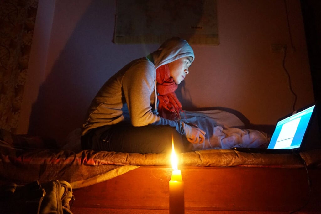 Junger Mann sitzt im Winter in einem dunklen Zimmer in Kathmandu und arbeitet bei Kerzenlicht während eines Load-Shedding-Abends.
