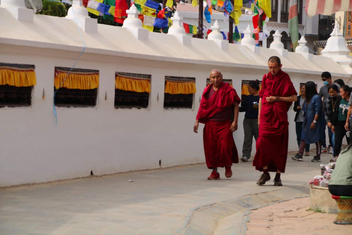 Buddhistische Mönche gehen im Alltag an einer Stupa in Nepal vorbei – Buddhismus als gelebte Praxis.