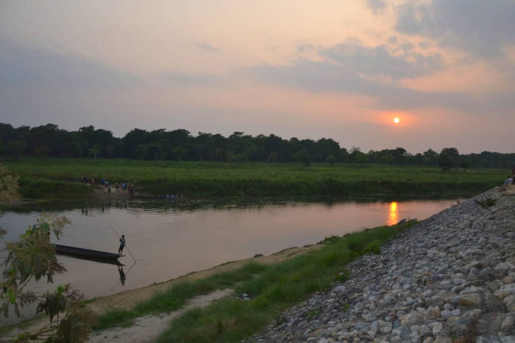 Flusslandschaft im Chitwan-Nationalpark bei Sonnenuntergang mit Boot und Ufervegetation