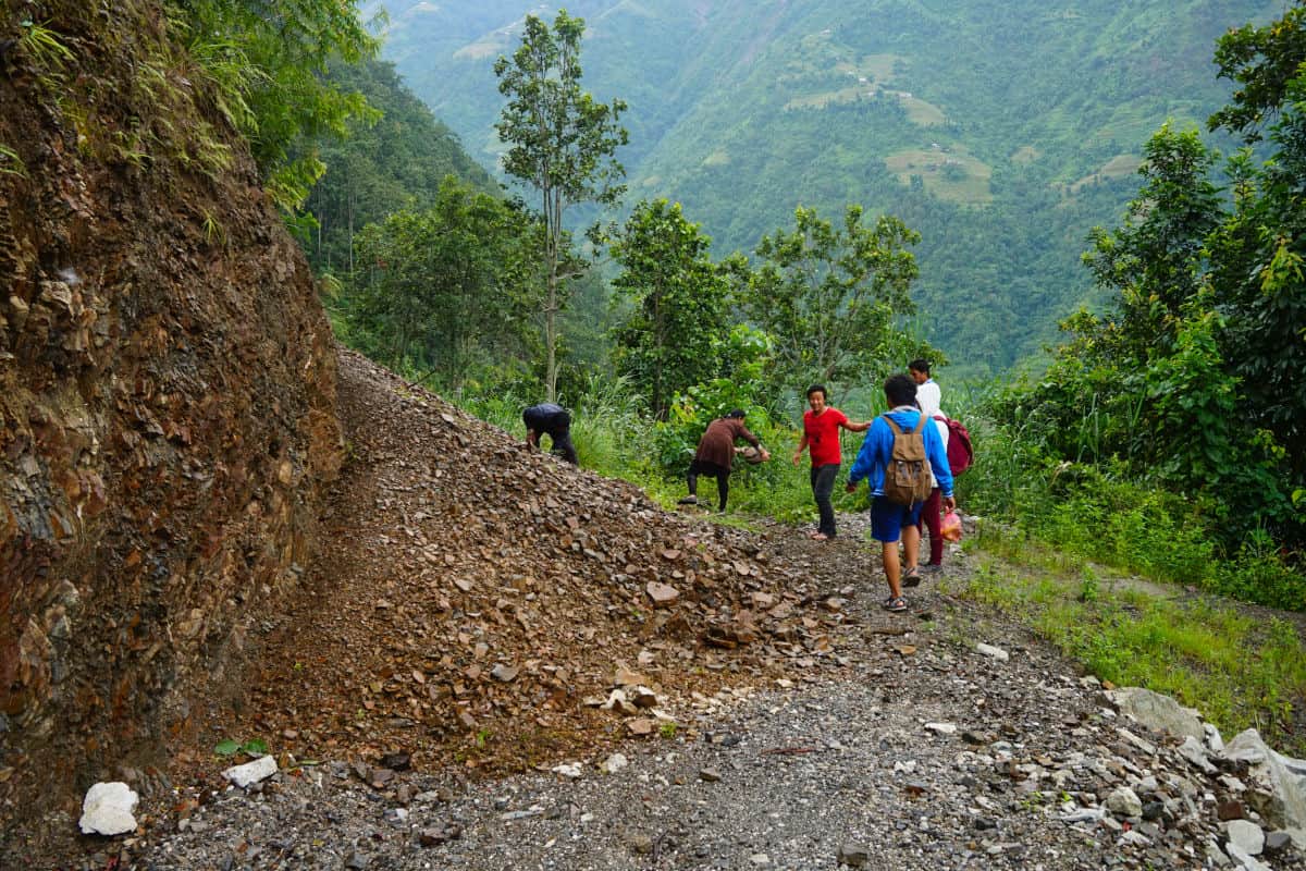 Menschen räumen Geröll von einer Dorfstraße im Mittelgebirge Nepals während der Monsunzeit