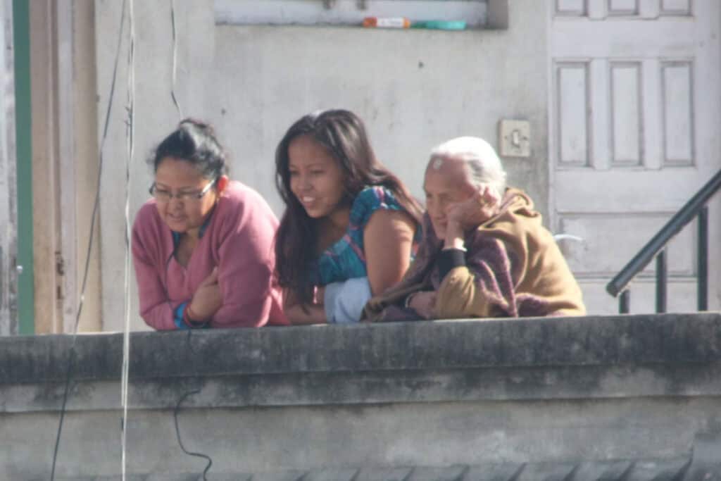 Drei Generationen einer nepalesischen Familie sitzen gemeinsam auf einem Balkon und beobachten den Alltag.