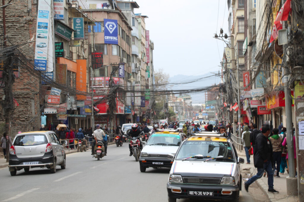 Alltäglicher Straßenverkehr in Kathmandu mit Autos, Motorrädern und Fußgängern