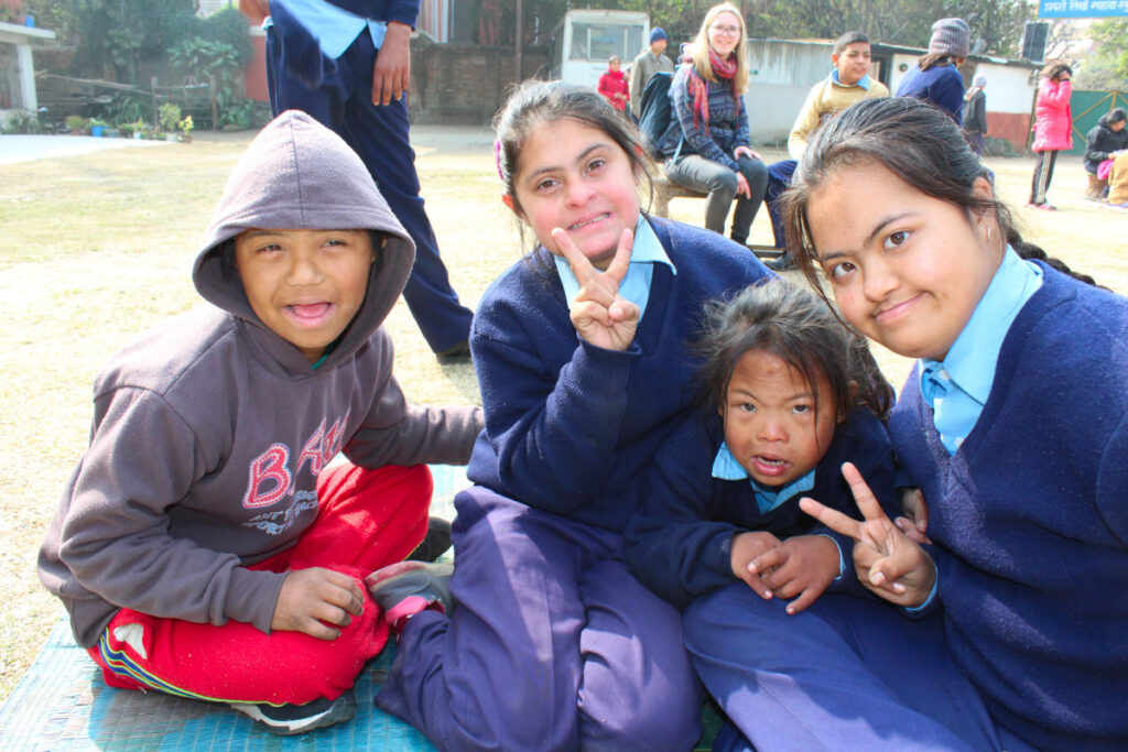 Schülerinnen und Schüler einer nepalesischen Schule sitzen gemeinsam im Schulhof und lächeln in die Kamera