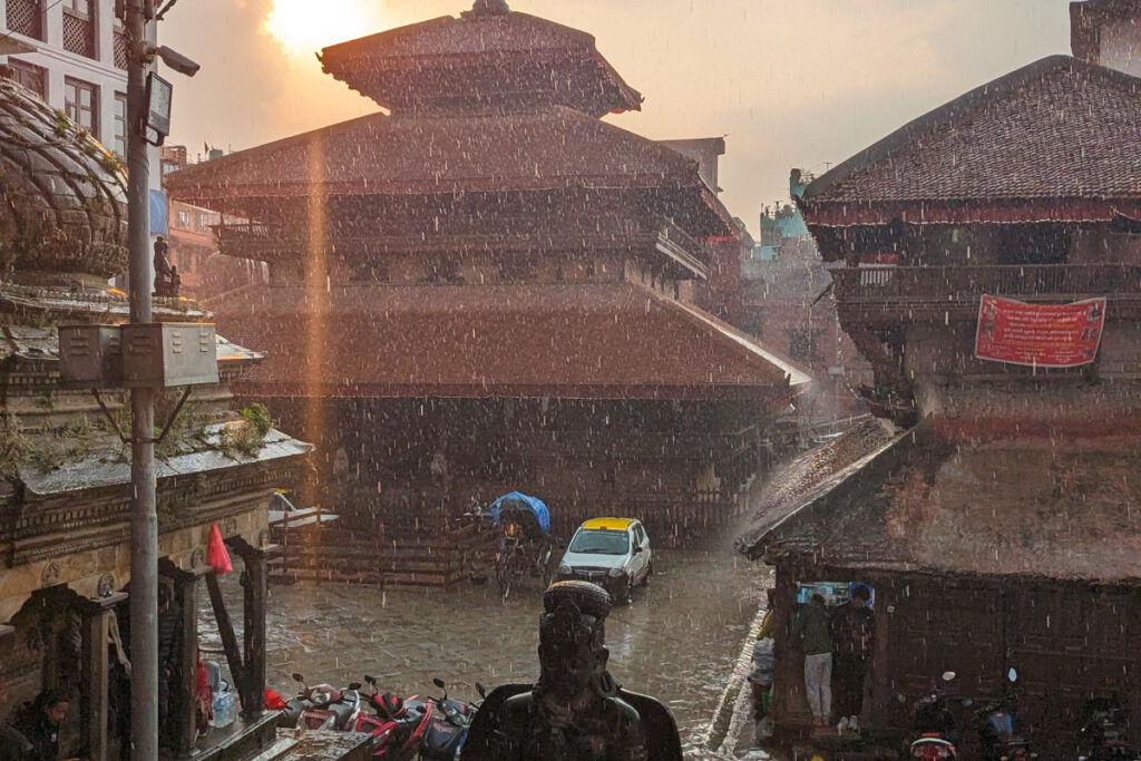 Alltag in Kathmandu im Regen Regenszene in Kathmandu mit Tempelarchitektur, Menschen mit Schirmen und nasser Straße