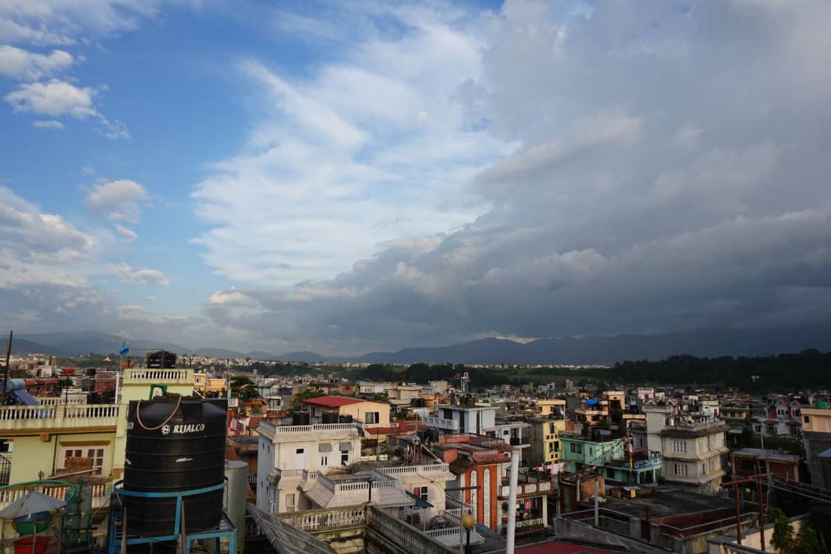 Blick über ein dicht bebautes Stadtviertel in Kathmandu mit Wohnhäusern, Dächern und Bergen im Hintergrund