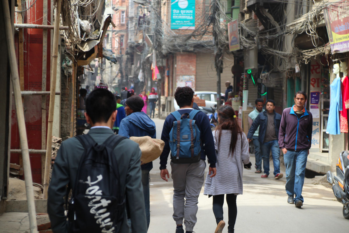 Menschen unterwegs in einer belebten Straße in Nepal mit Häusern, Kabeln und Alltagsleben