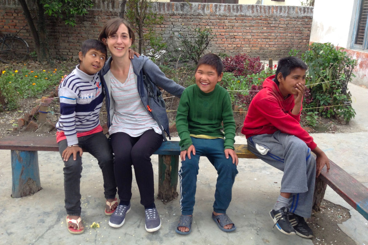 Freiwillige sitzt mit nepalesischen Jugendlichen auf einer Bank im Schulhof