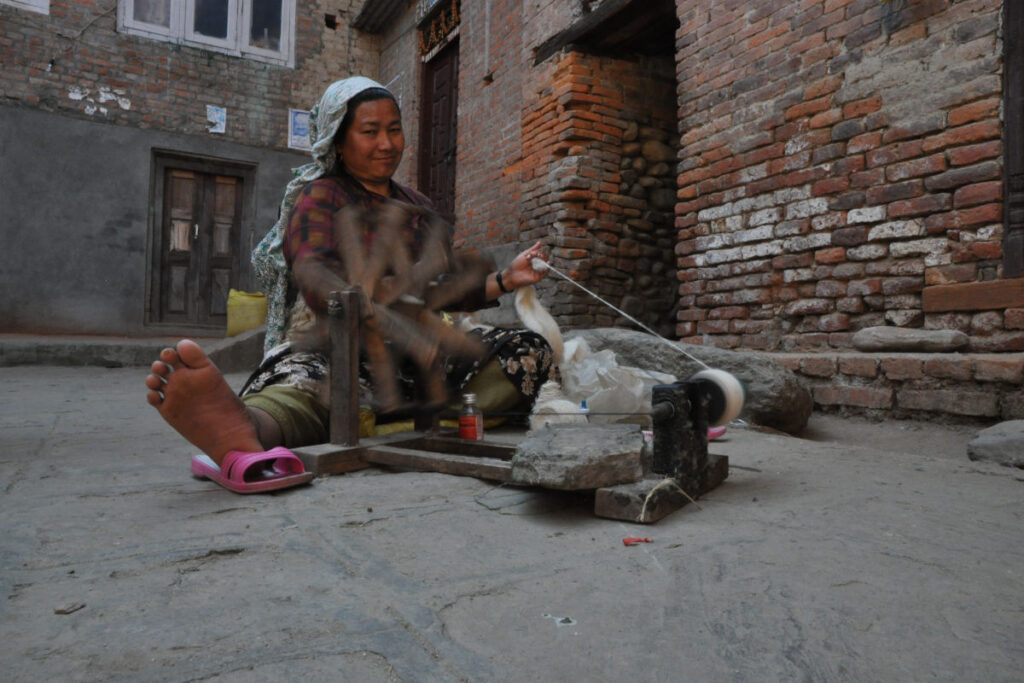 Handwerkliche Arbeit in Nepal | meinNepal Nepalesische Frau spinnt Garn mit traditionellem Handspinnrad in einem Dorfhof