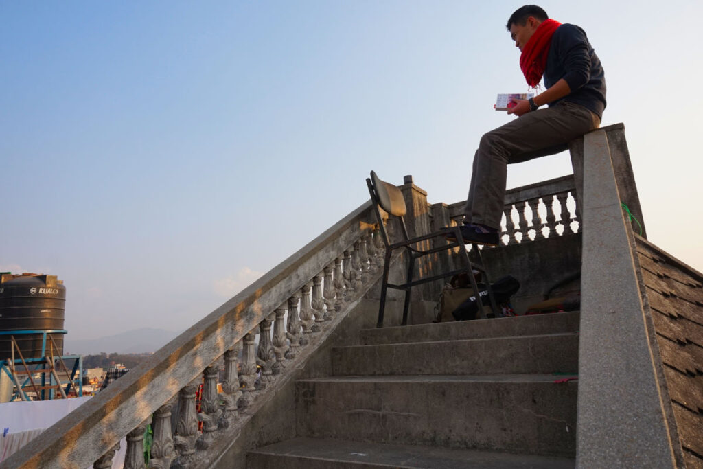 Person sitzt auf einer Dachterrasse in Kathmandu und liest mit Blick über die Stadt