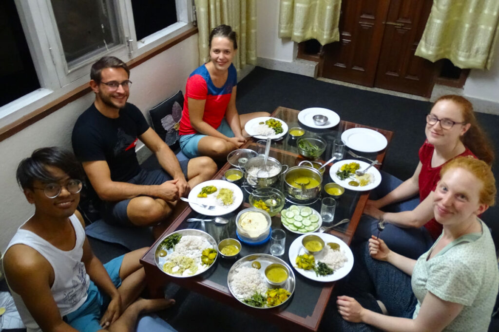 Gruppe sitzt gemeinsam beim Abendessen auf dem Boden und isst traditionell nepalesisches Essen