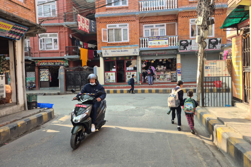 Straßenszene in Kathmandu mit Schulkindern und Motorroller im morgendlichen Alltag