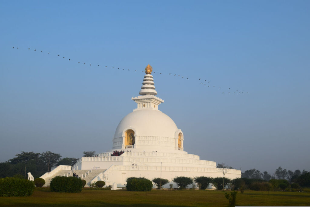 Weiße Friedensstupa in Lumbini mit weiter Grünfläche und klarem Himmel