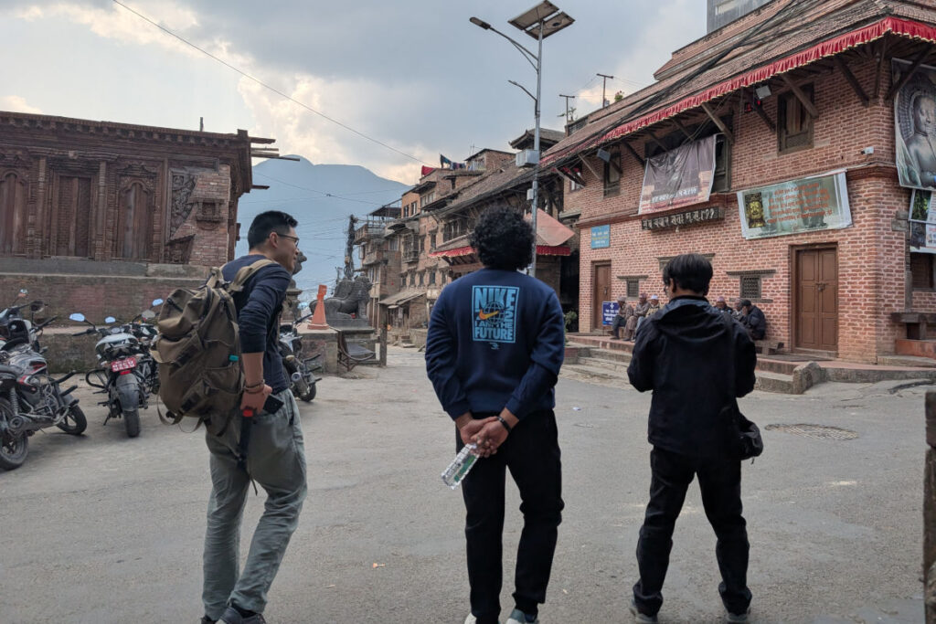 Drei Menschen im Gespräch auf einer Straße vor traditionellen Backsteingebäuden in Kathmandu