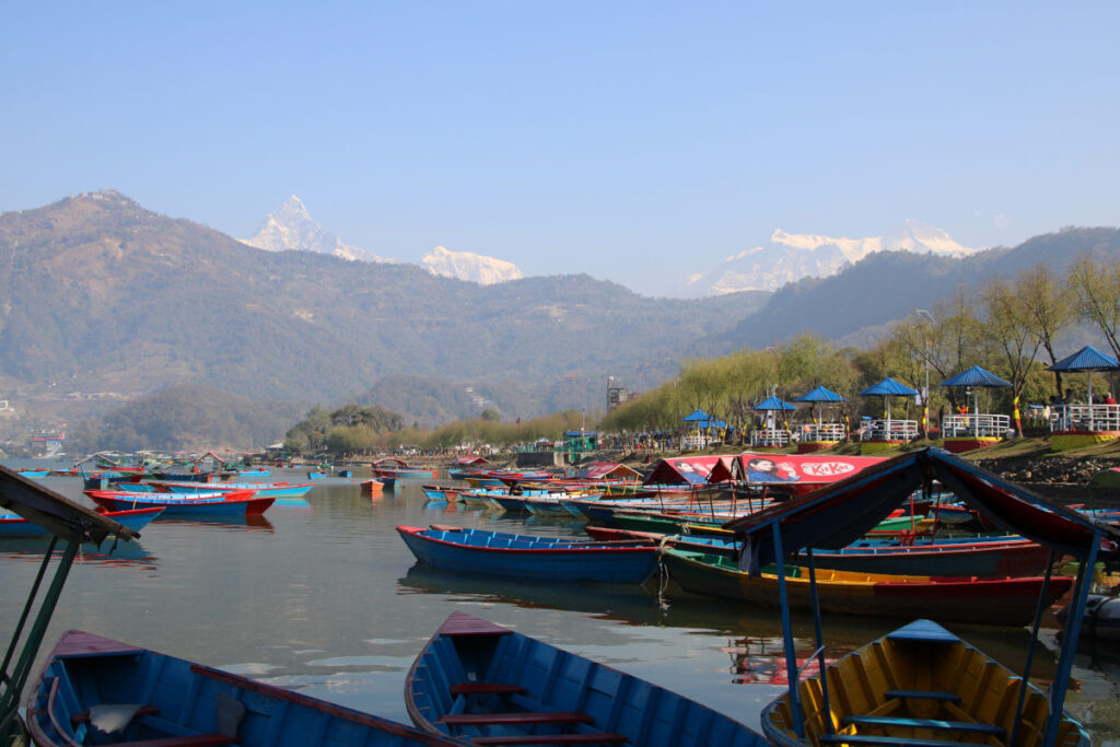 Bunte Ruderboote am Ufer des Phewa-Sees in Pokhara mit Blick auf die Berge