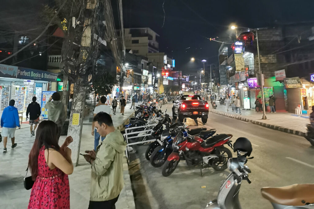 Belebte Straße in Lakeside Pokhara bei Nacht mit Bars, Shops und Motorrädern