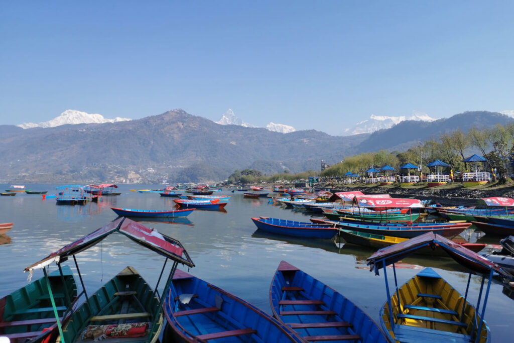 Bunte Boote am Ufer des Phewa-Sees in Pokhara mit Bergen im Hintergrund