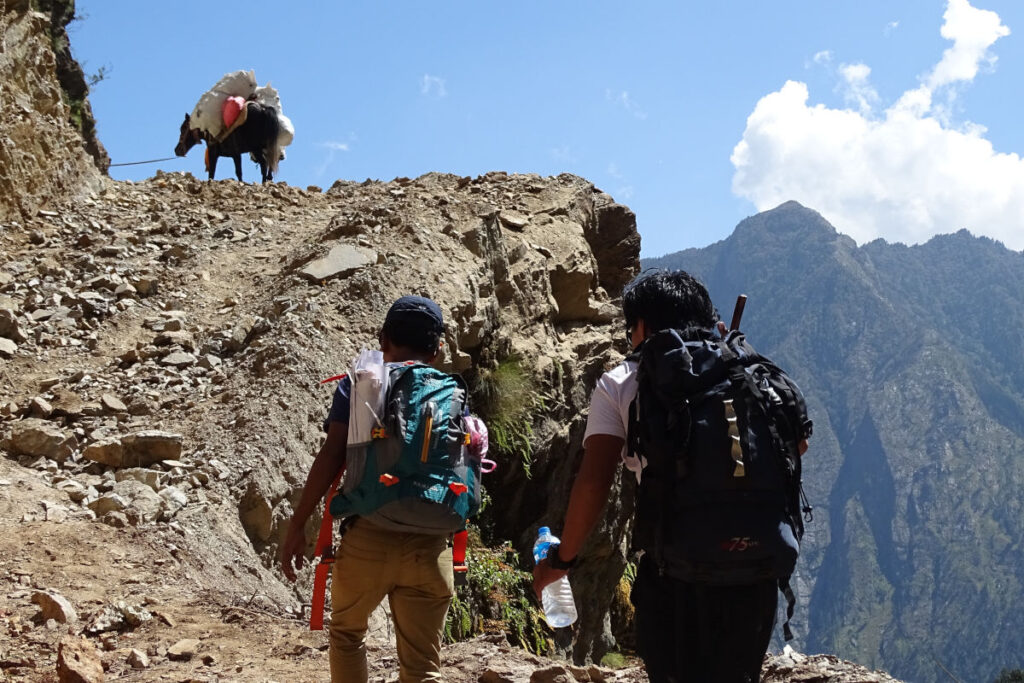 Zwei Trekker auf einem schmalen Bergpfad in Nepal mit steilem Gelände und Gepäck