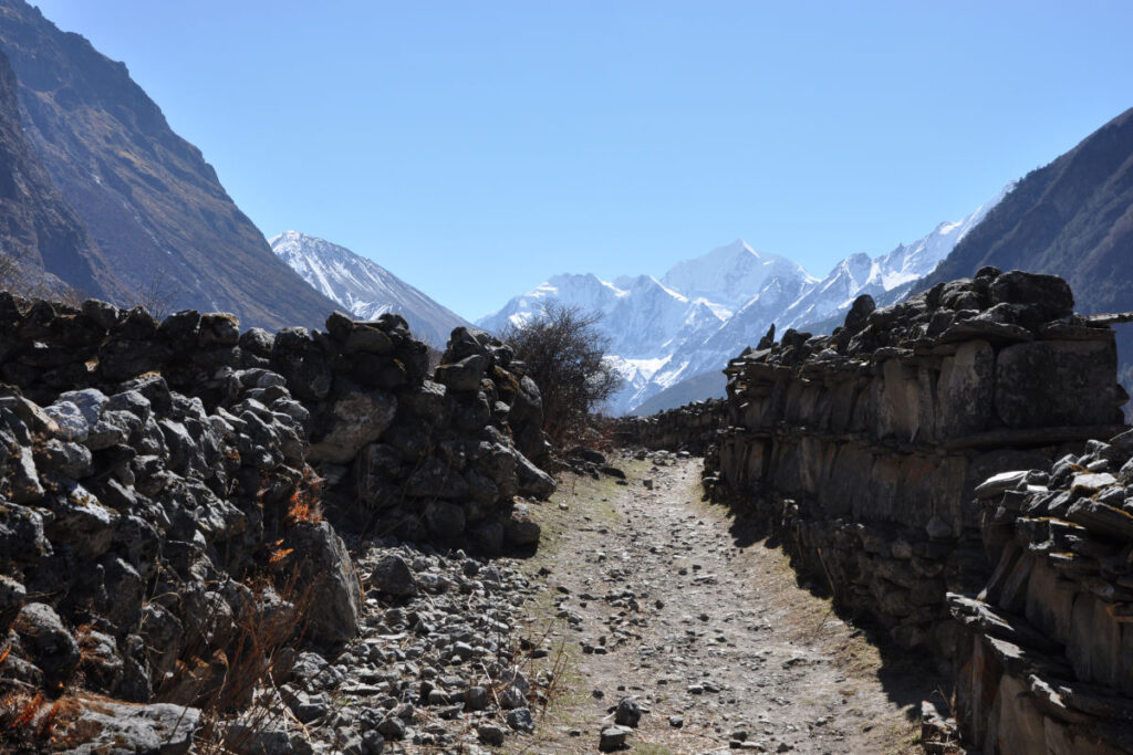 Schmaler Wanderweg zwischen Steinmauern mit Blick auf Himalaya-Berge
