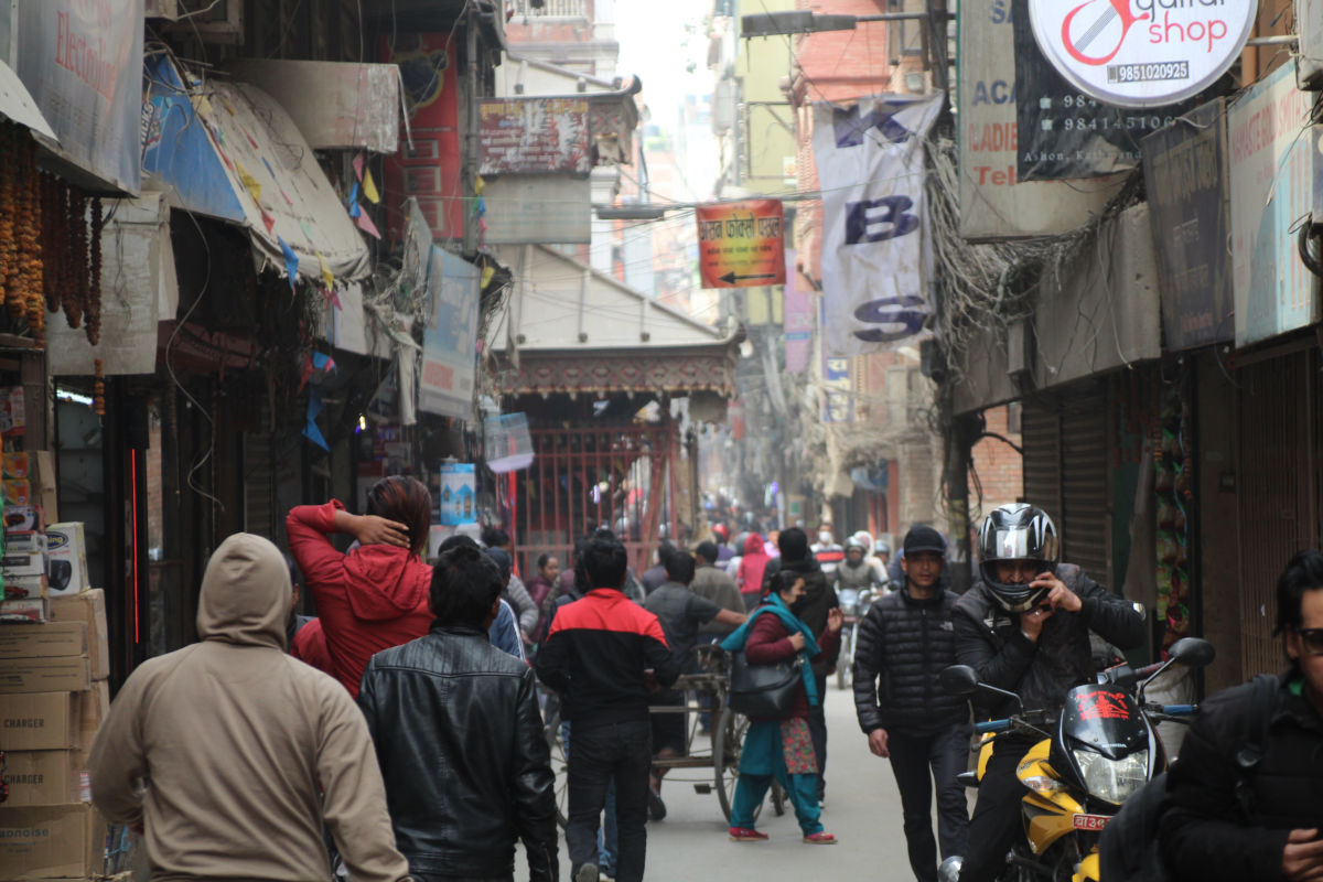 Belebte enge Straße in Kathmandu mit Menschen, Motorrädern und Geschäften