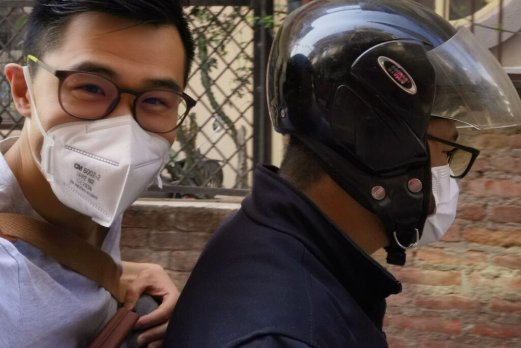 Zwei Personen fahren mit dem Motorrad durch Kathmandu und tragen Schutzmasken