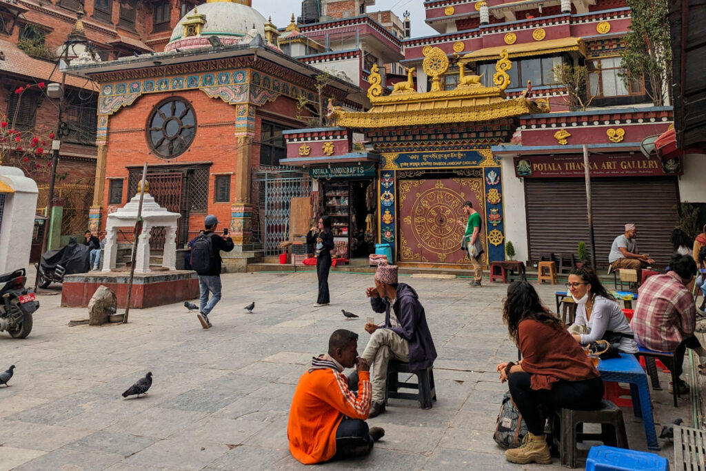 Menschen sitzen entspannt auf einem Platz in Kathmandu vor Tempelgebäuden