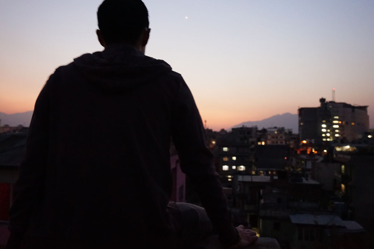 Person allein auf einer Dachterrasse mit Blick über Kathmandu bei Abenddämmerung