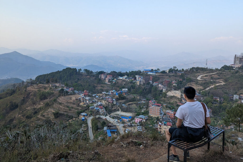 Person sitzt auf einer Bank und blickt bei Sonnenaufgang über Bandipur in Nepal