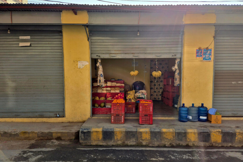 Kleiner Laden in Nepal mit Obstkisten und Bananen vor einem halb geöffneten Rolltor