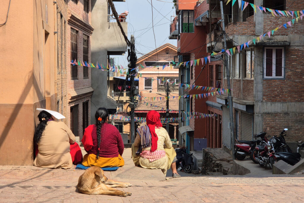 Frauen sitzen in einer Straße in Nepal mit dem Rücken zur Kamera und schauen in die Gasse