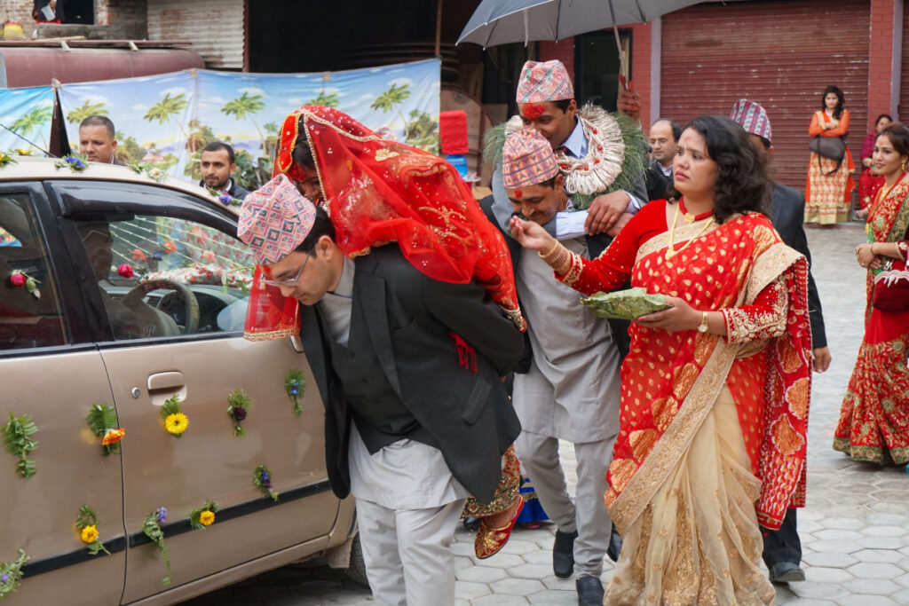 Braut wird bei einer traditionellen Hochzeit in Nepal zum Auto getragen, während Familie sie verabschiedet