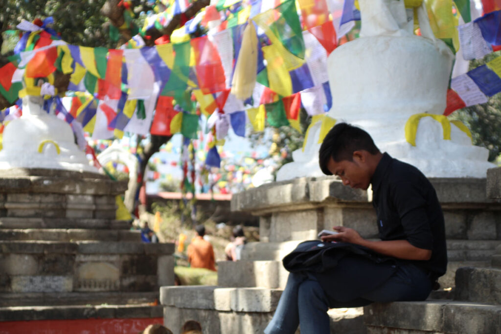 Junger Mann nutzt Smartphone bei Stupas mit Gebetsfahnen in Nepal