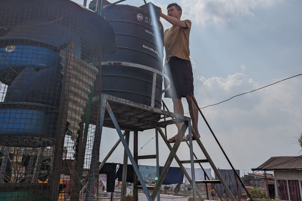 Person prüft Wasserstand in Wassertank auf einem Hausdach in Kathmandu