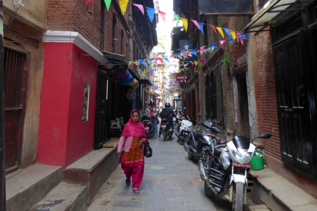 Unterwegs in den Gassen von Patan Enge Altstadtgasse in Patan mit einer Frau, Motorrädern und traditionellen Backsteinhäusern