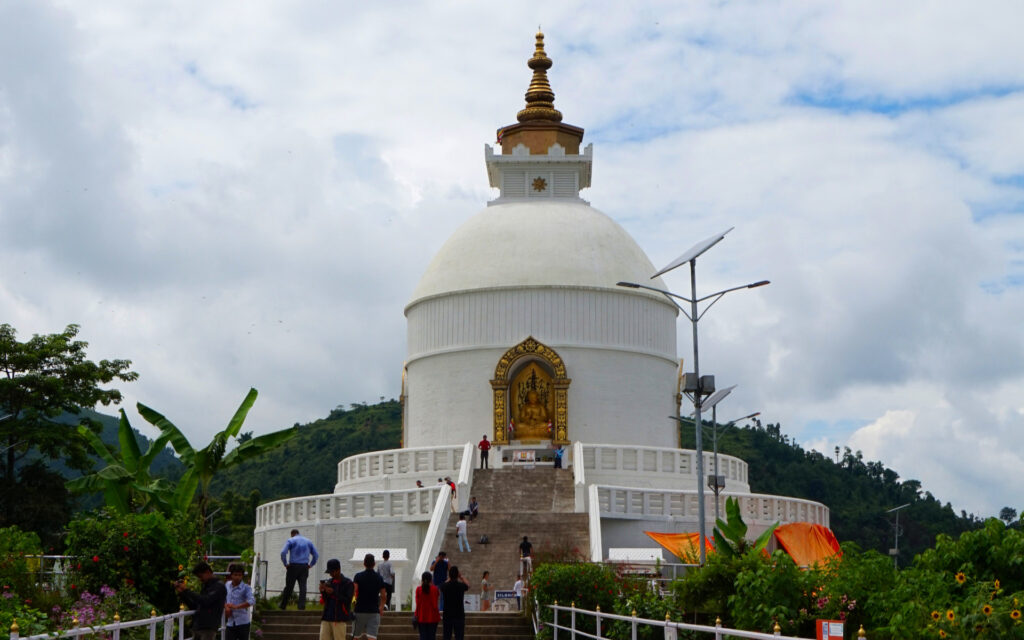 Peace Pagoda in Pokhara Die weiße Peace Pagoda in Pokhara mit goldener Spitze, Buddha-Nische und Besuchern auf den Treppen vor dem Stupa.
